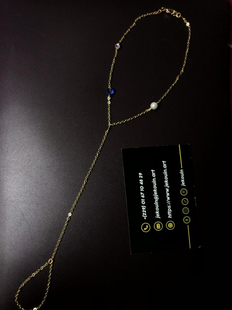 Bracelet de pied en perles de rocaille chaînées à la main, alternant une chaînette dorée et des perles violettes transparentes, lavande nacré, avec un fermoir mousqueton en métal doré. Une carte de visite noire de « Jekouin.art » avec logos dorés est placée à coté.