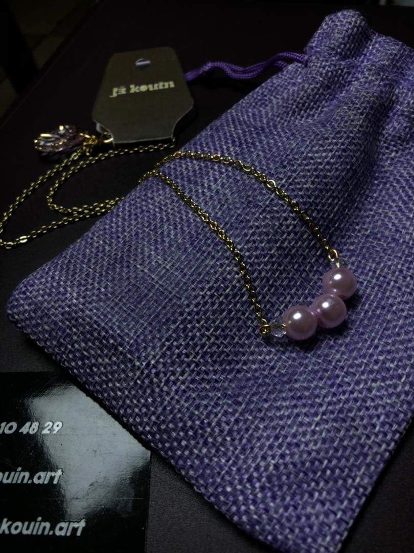 Collier fin avec une chaîne dorée présentant deux pendentifs distincts de couleur violette, conçus pour être interchangeables. L'un est un pendentif violet en forme de coquillage, l'autre est un pendentif violet constitué de trois perles nacrées assorties.