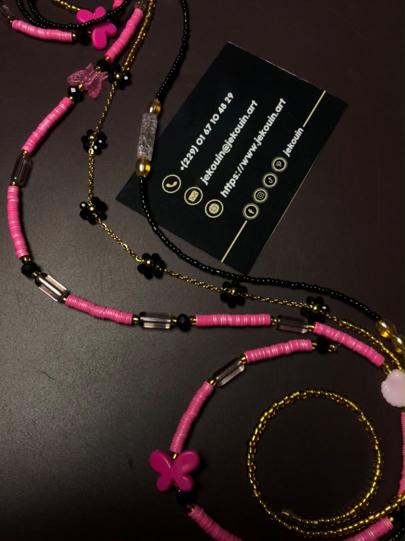 Vue d'ensemble d'un baya de taille disposé en vagues sur fond noir mat, composé de perles roses et noires avec un pendentif fée dorée à côté d'une carte jǯ kouin.