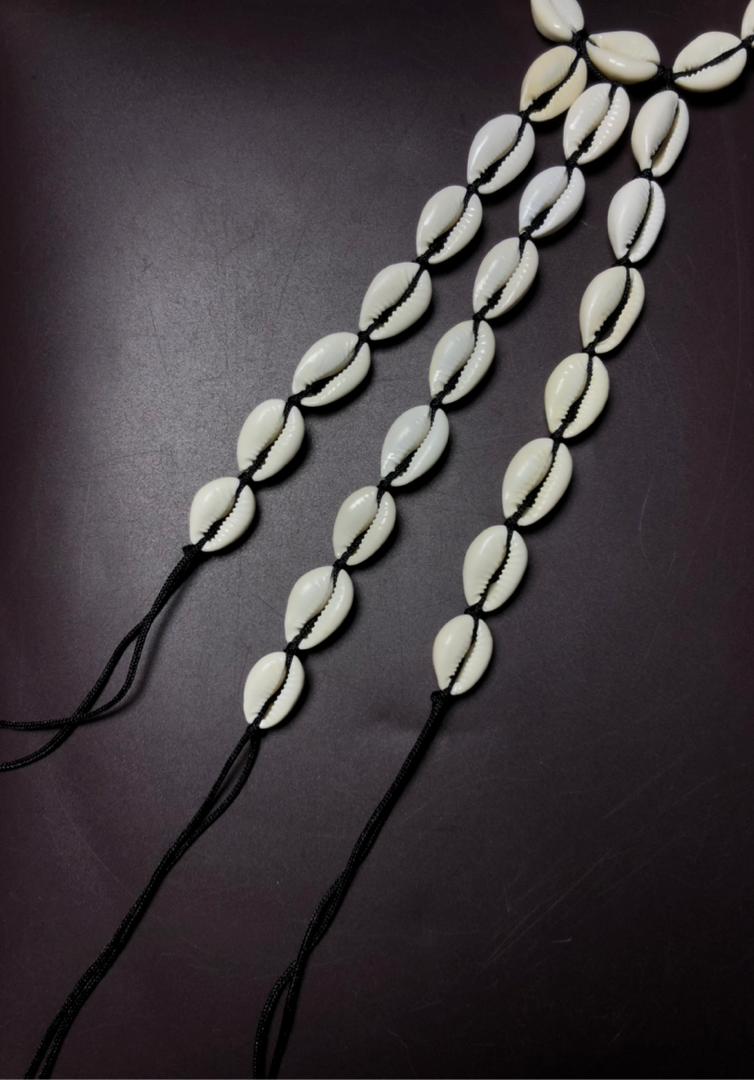 Gros plan vertical sur trois rangées parallèles de coquillages cauris blancs reliés par des nœuds de fil noir.