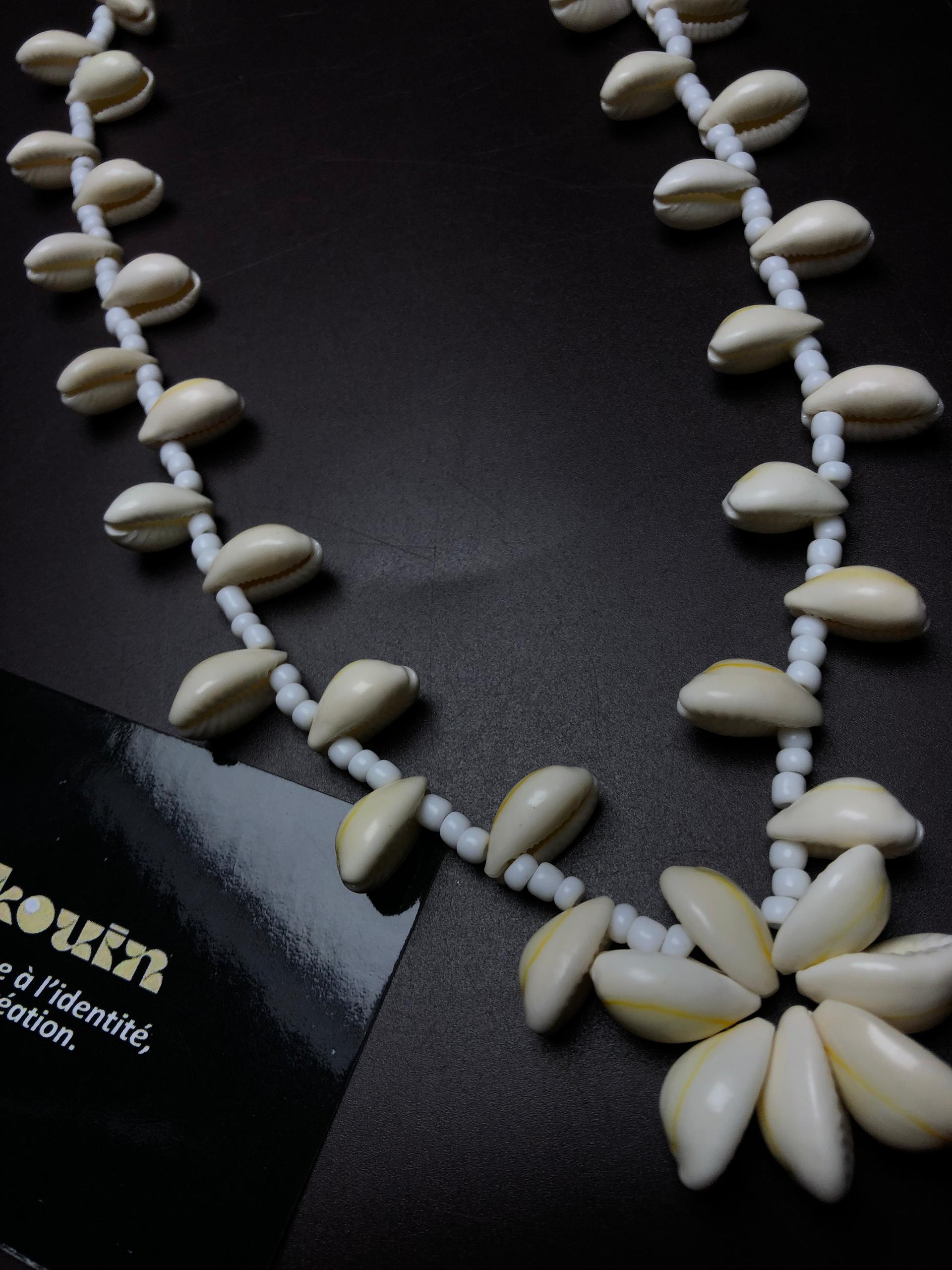 Gros plan sur le pendentif en forme de fleur fait de coquillages cauris et sur le détail des perles blanches du collier jekouin.