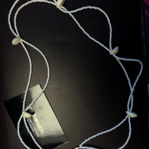 Une parure de tête ou diadème composé de rangs de micro-perles blanches entrelacées et orné de coquillages cauris, disposé sur fond noir avec la carte jekouin.