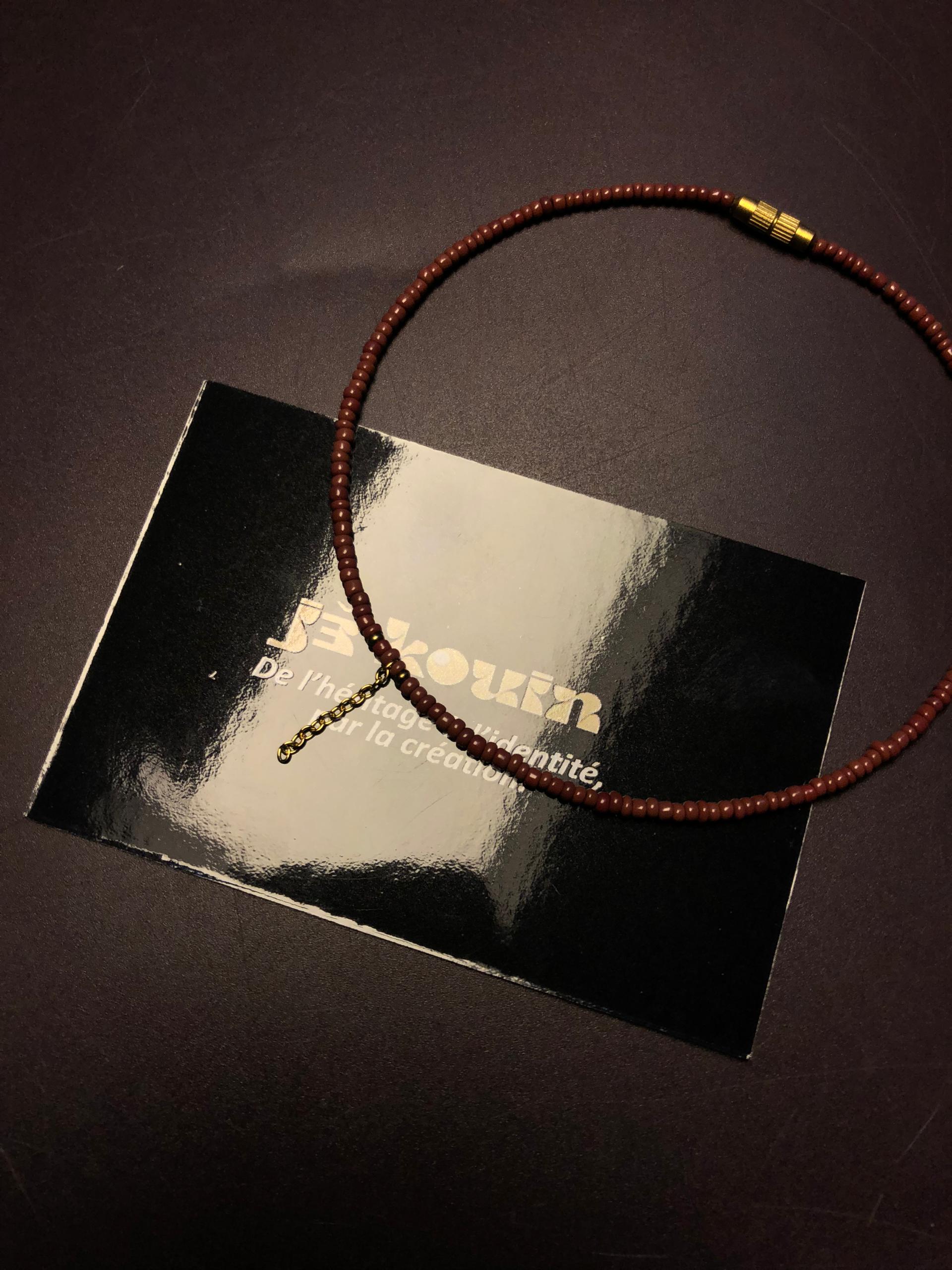 Chaîne de cheville en fines perles de rocaille terracotta avec pampille dorée et fermoir à vis, posée sur la carte noire jekouin.