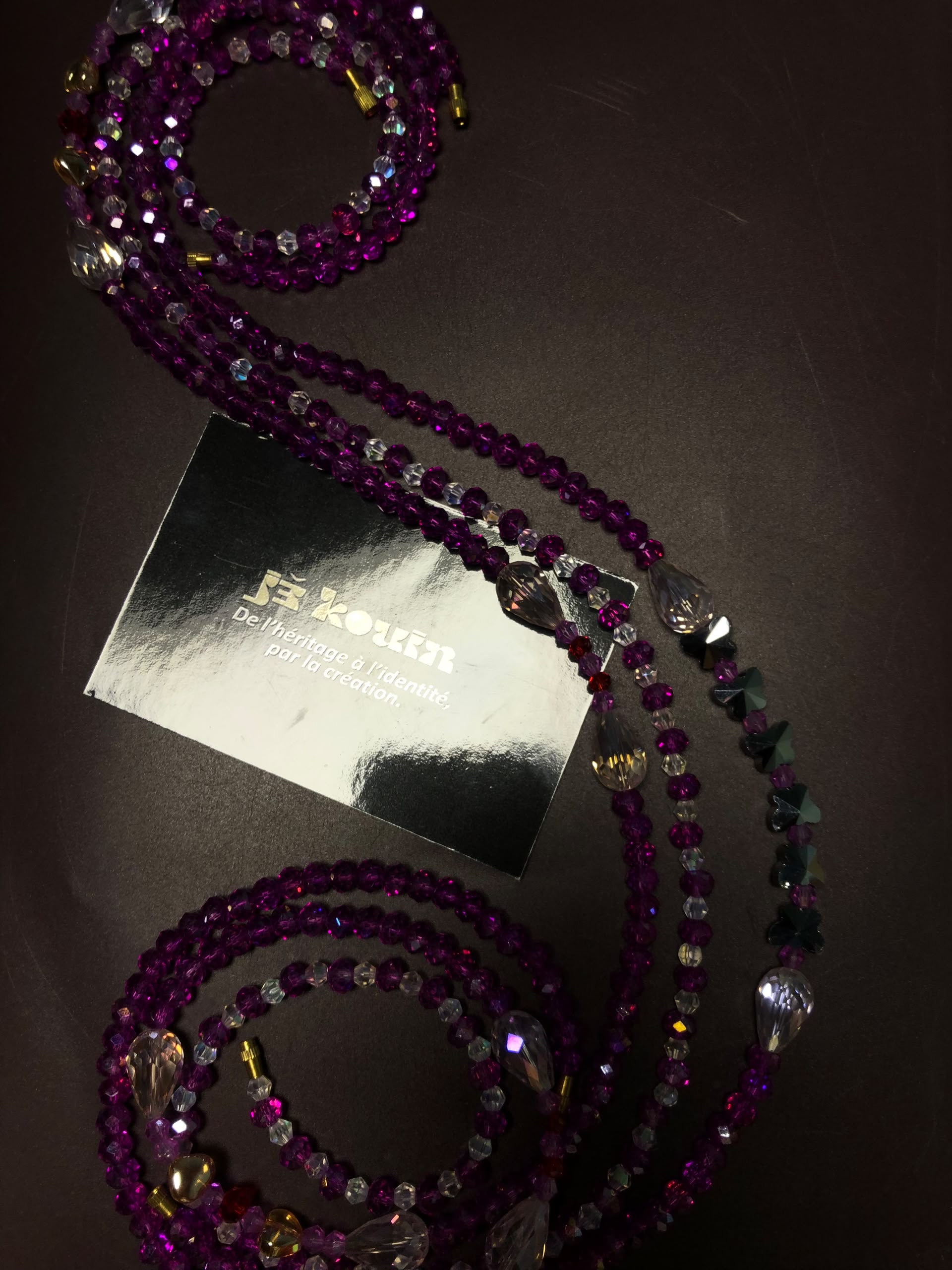 Chaîne de taille baya en cristal violet intense avec pendentifs gouttes en verre translucide ondulant autour d'une carte de visite jekouin.