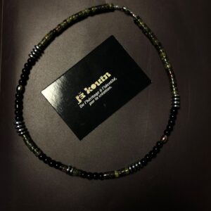 Collier ras-de-cou mixte composé de perles cylindriques vertes, rondes noires et hématite métallisée, entourant la carte jekouin sur fond sombre.